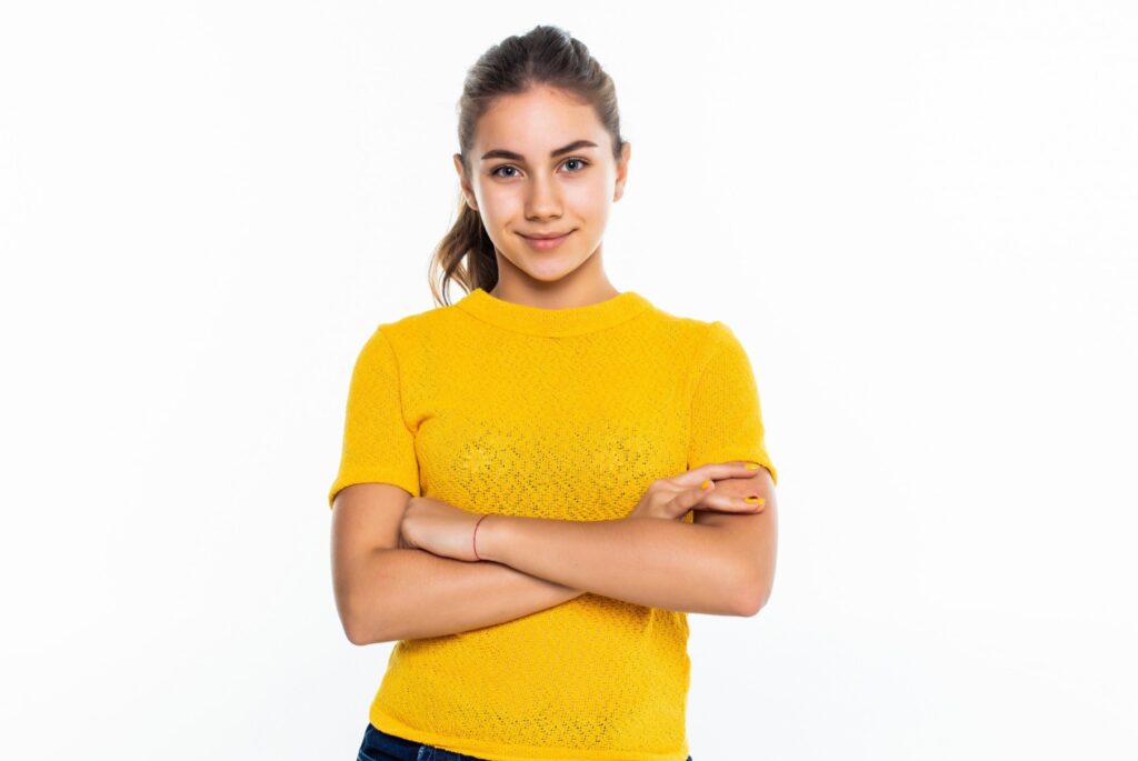 Beautiful teen girl student with confident expression, keeps arms folded. portrait of smiling teenager isolated on white wall