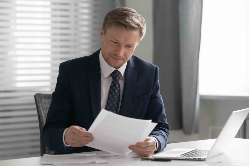 Businessman in suit reading formal letter in front of his laptop