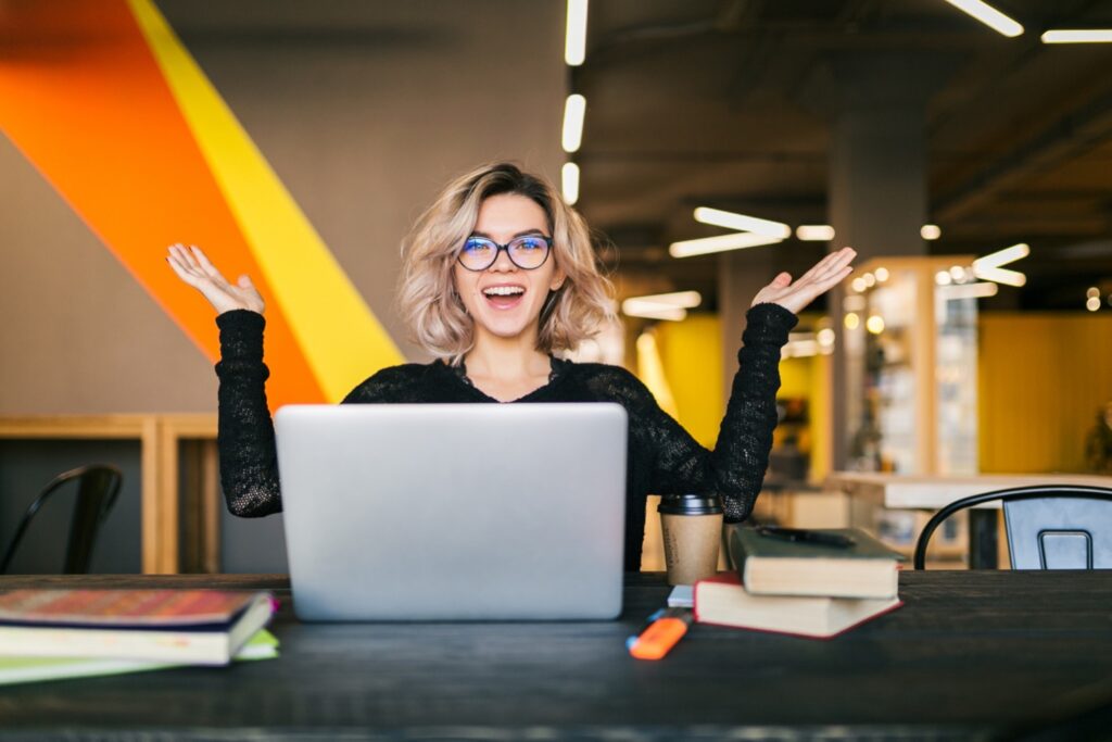 Happy and excited young job applicant in front of her laptop in coworking space