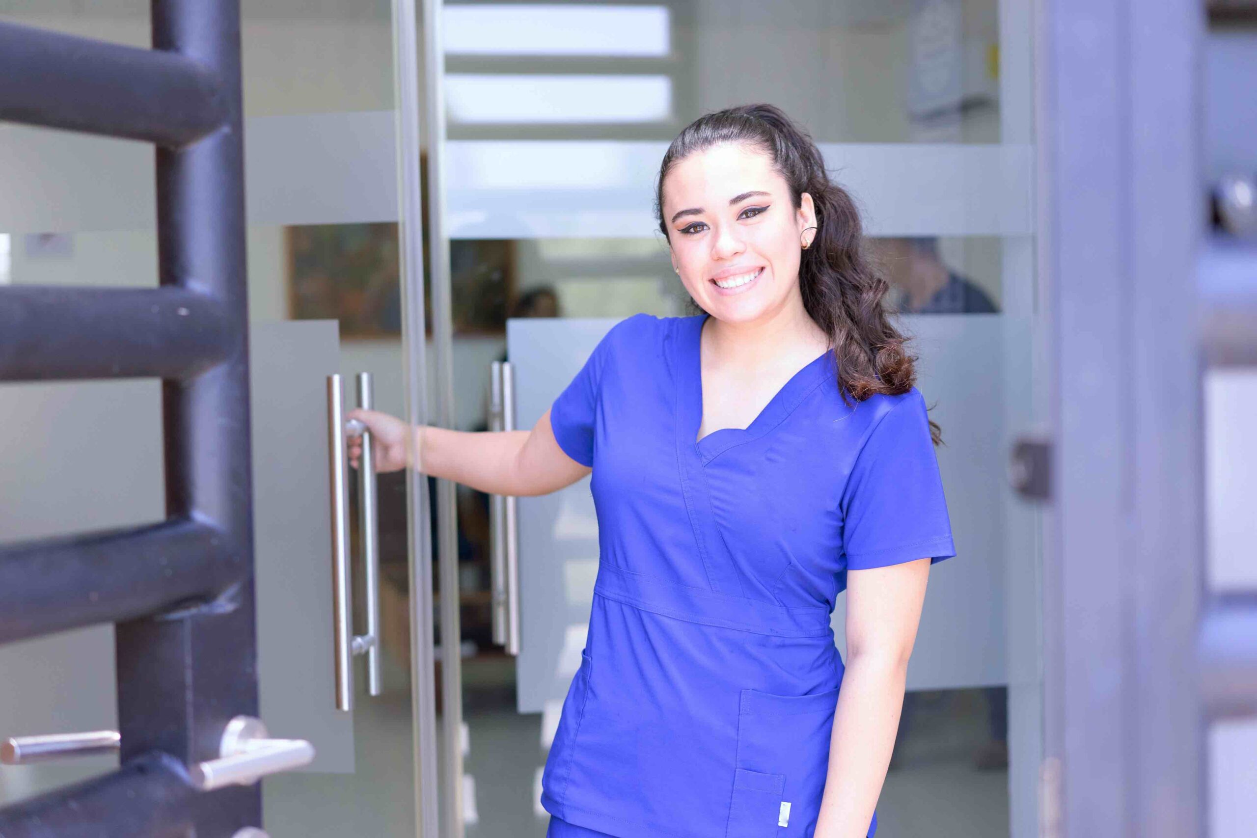Happy female certified medical assistant opening door to practice