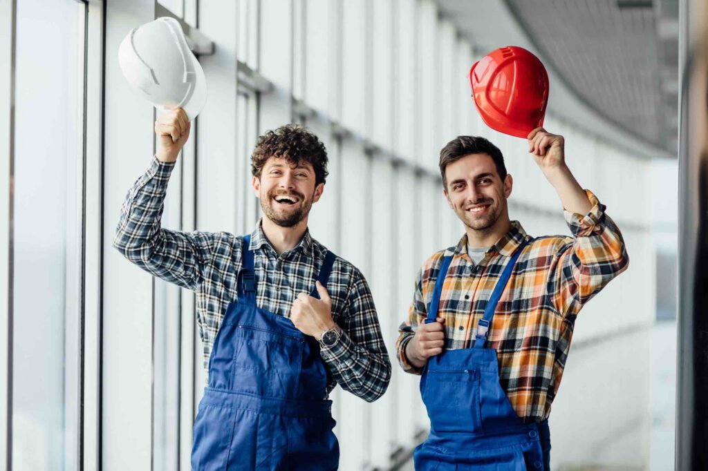 Happy male engineers waving with hats in construction attire