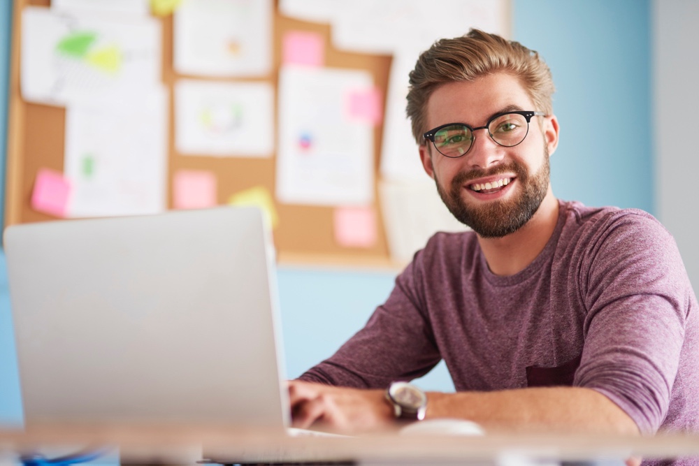 Happy young man with laptop and casual attire at office