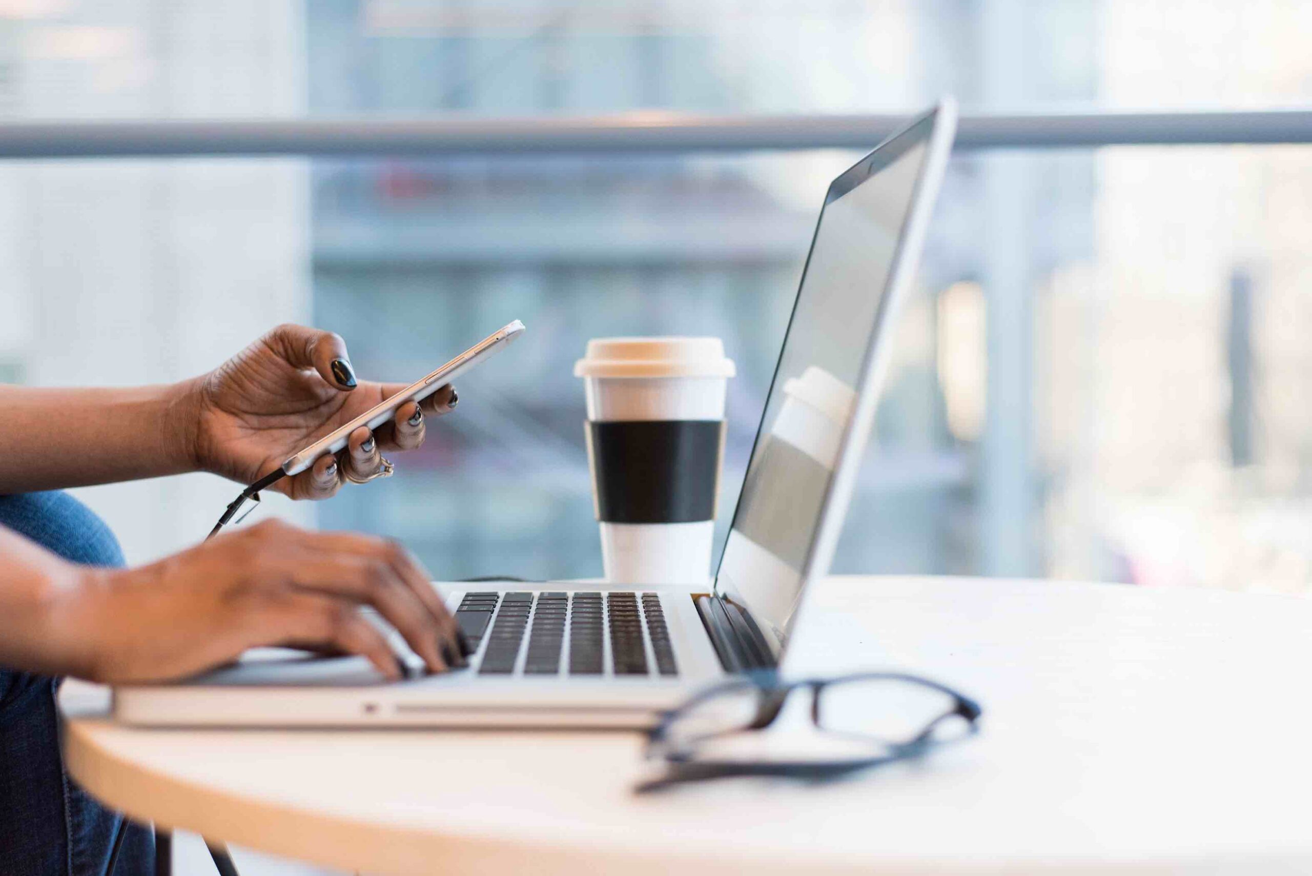 Job seeker typing her registered nursing resume on her laptop while holding phone