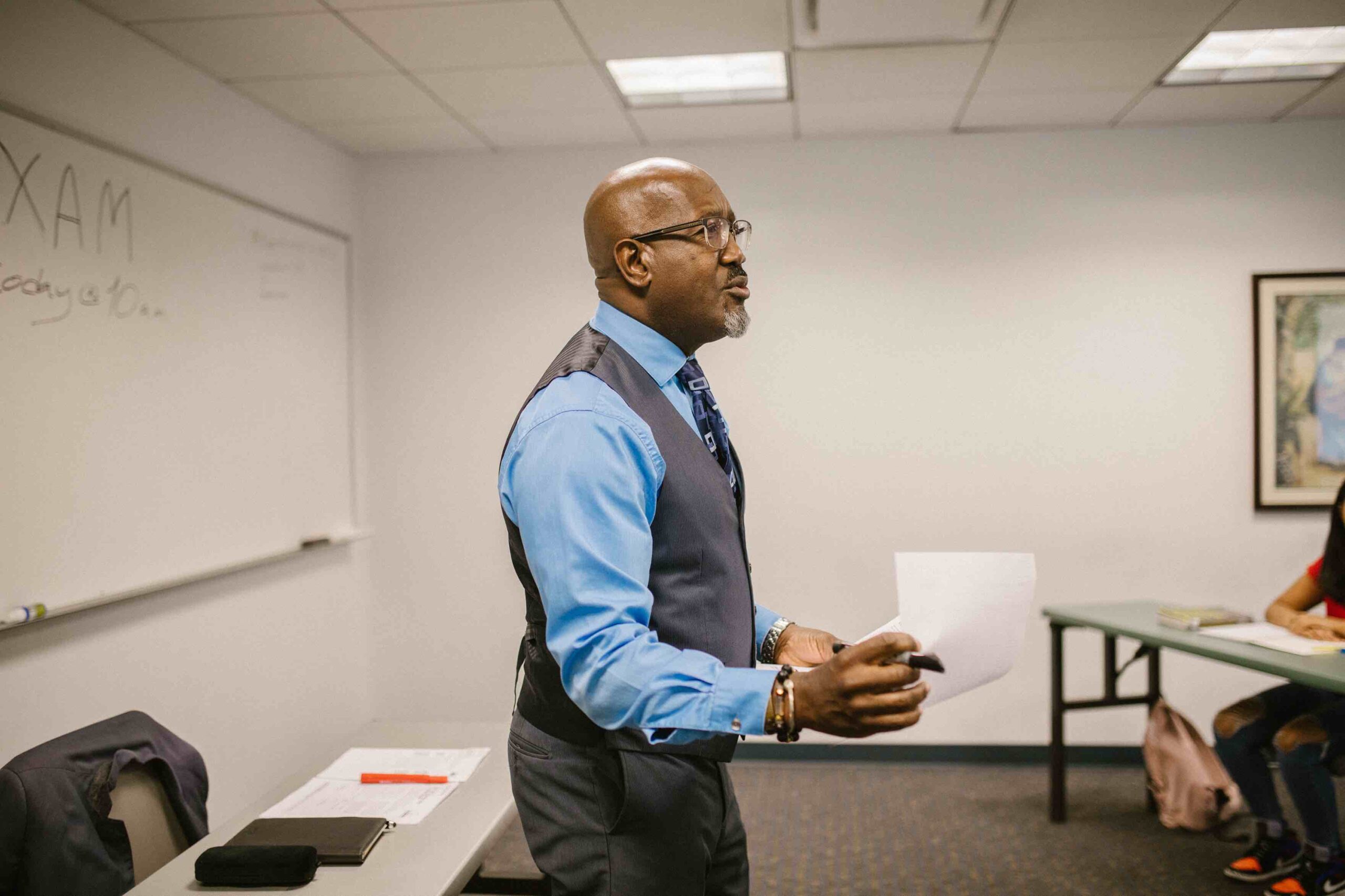 Male teacher in front of whiteboard handing out exam