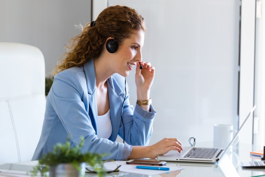 Smiling female customer service representative with headset on in front of her laptop