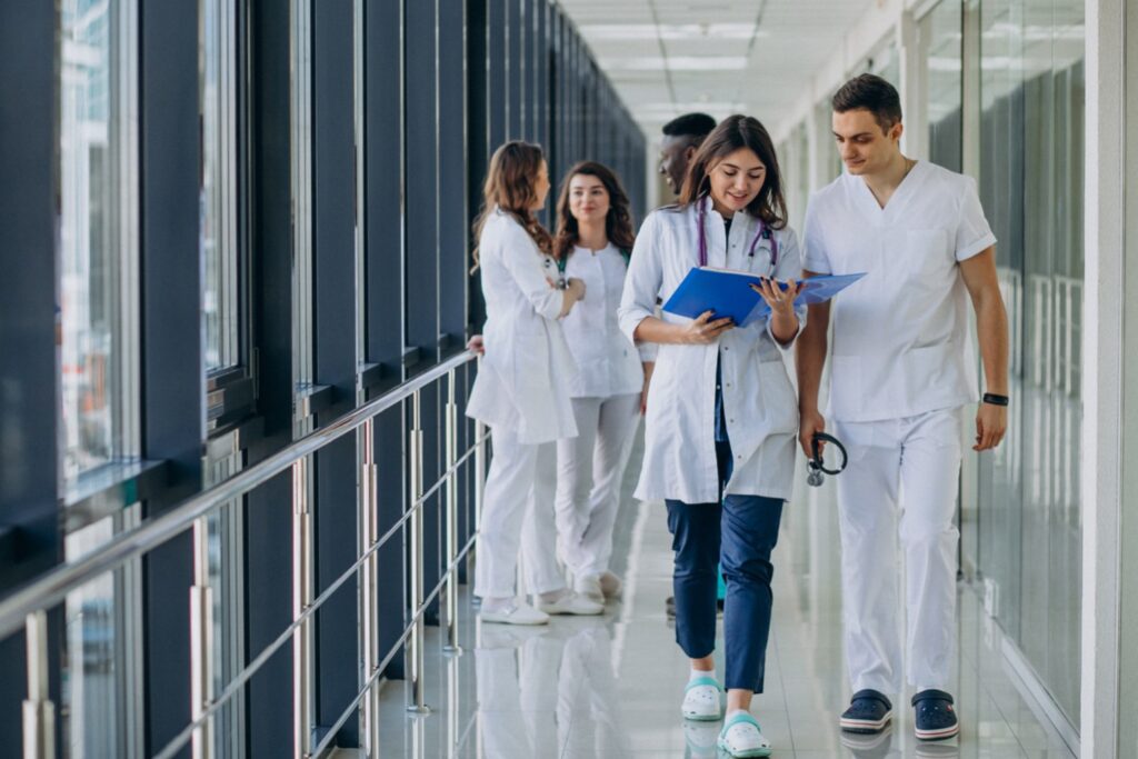 Two young medical assistants walking on hospital corridor checking out patient files