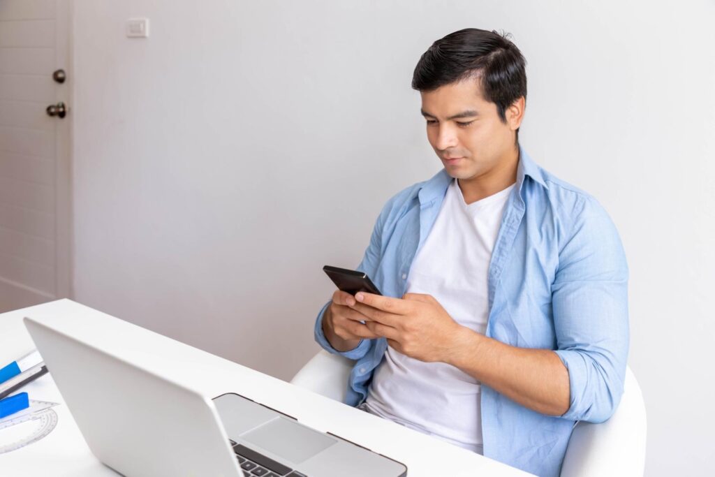 Young data entry clerk checking the correct data entry resume format on his phone in front of laptop