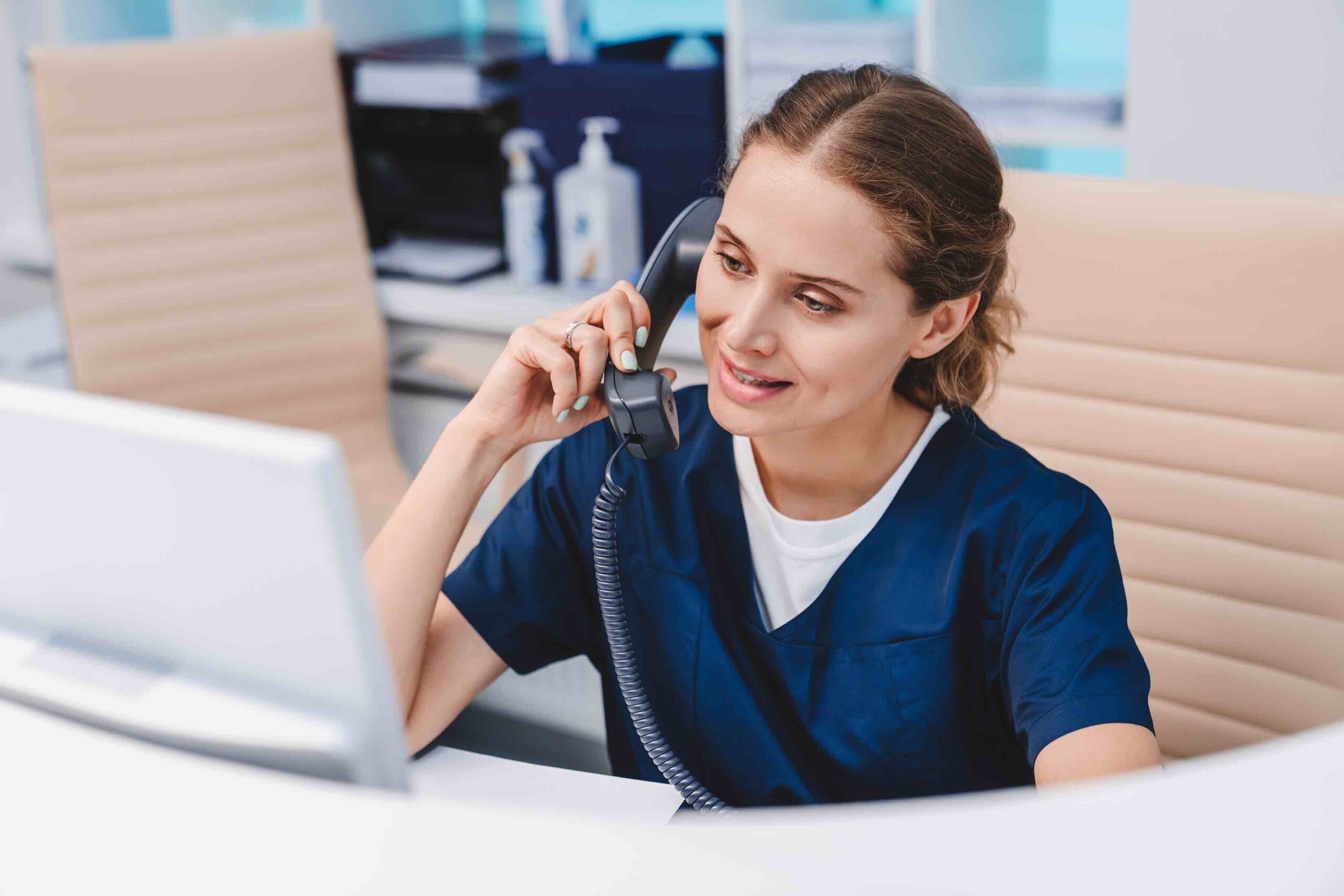 Young female medical assistant on phone while sitting and on PC monitor