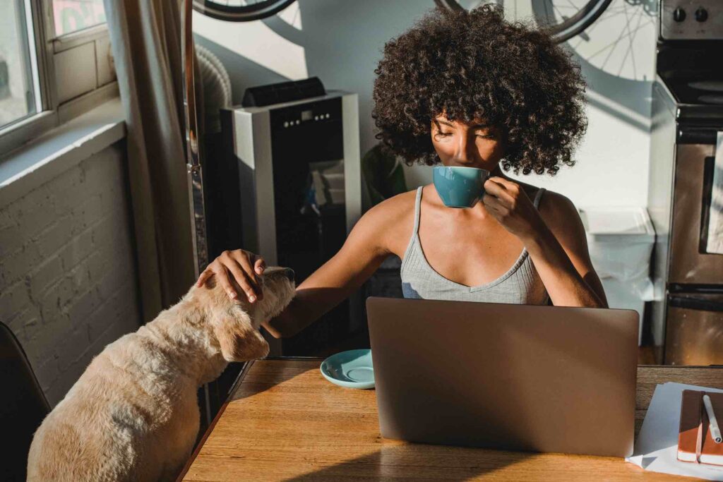 Young job applicant writing resume at home while drinking coffee and petting her dog
