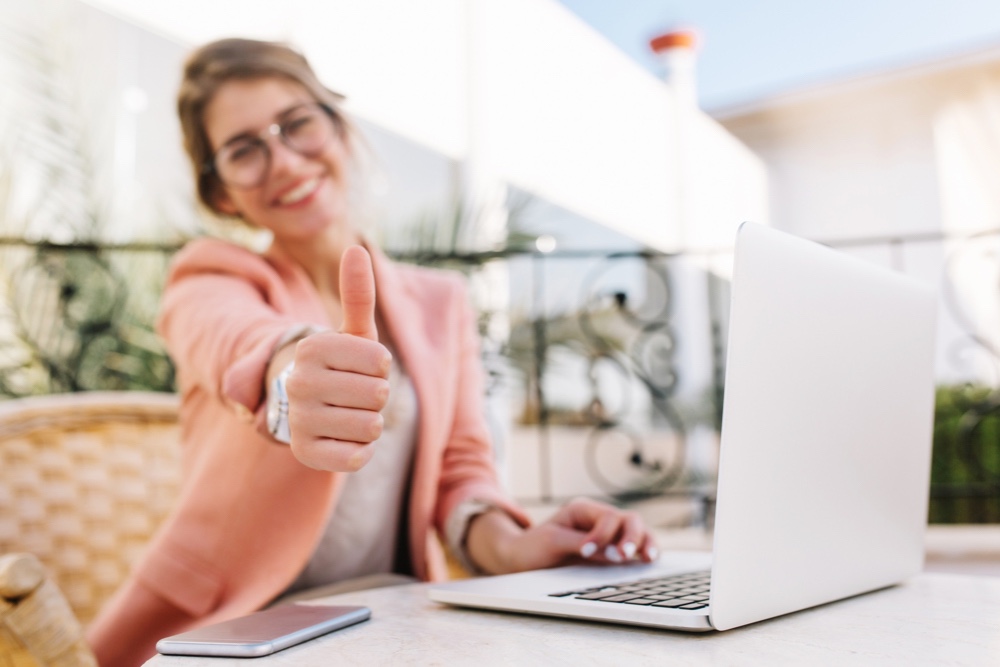Young woman in front of laptop wearing a business casual wardrobe thumbs up
