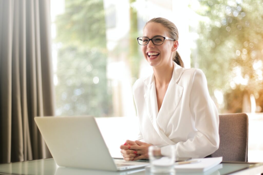 Laughing business woman sitting on a desk in front of a laptop