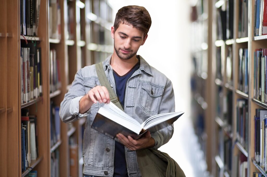 Male college student reading a book in the library