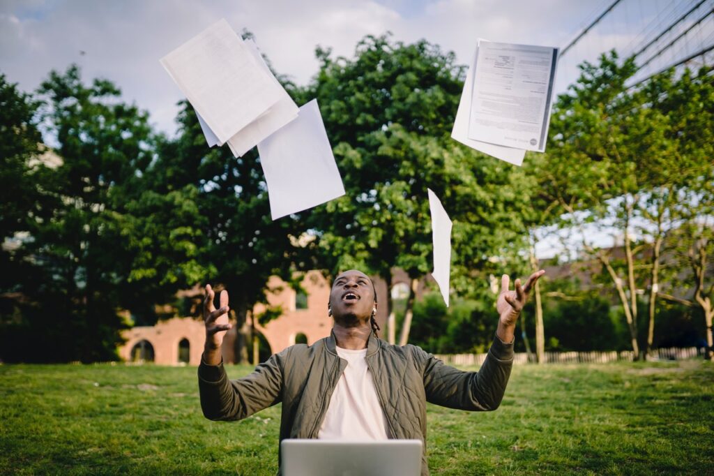 Male college student sitting on campus throwing papers in the air