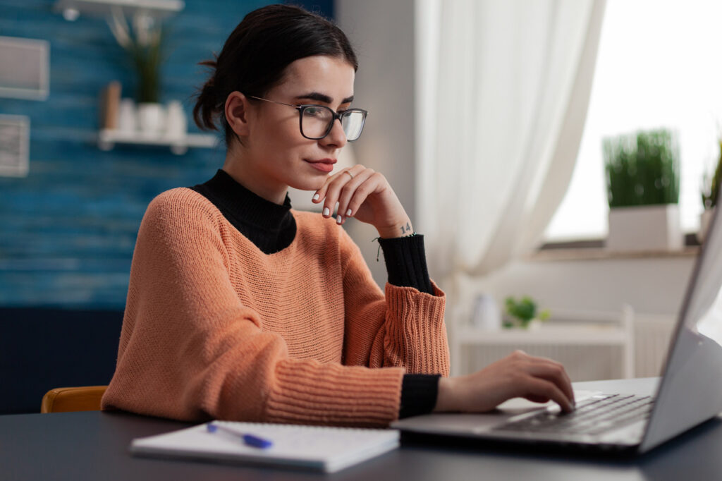 Female job applicant with glasses casually checking an interview response email on her laptop