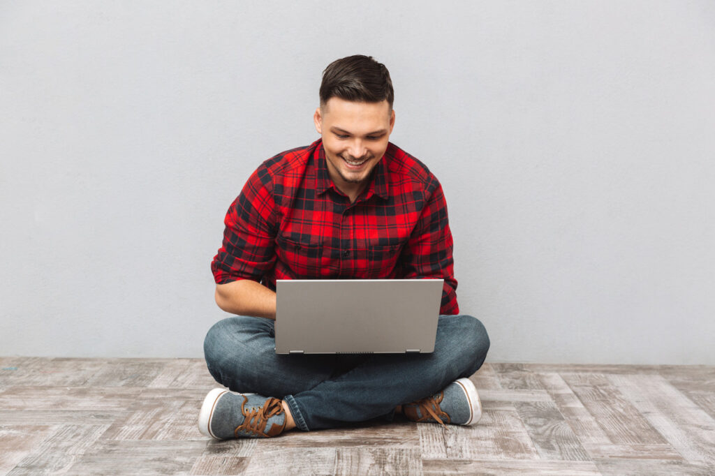 Smiling male job candidate writing a thank you email on a laptop while sitting on the floor