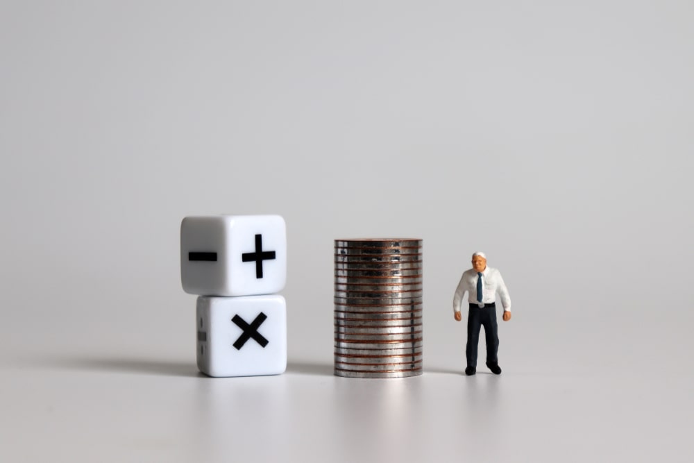 miniature man next to pile of coins next to mathematic cube