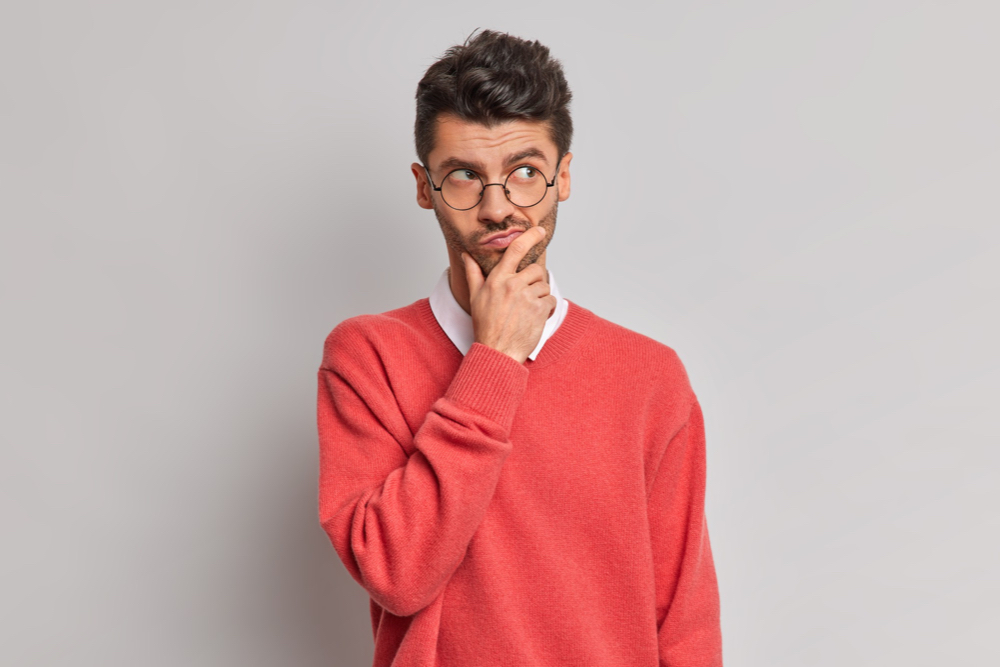 Thoughtful handsome adult man holds chin and looks pensively away tries to solve problem