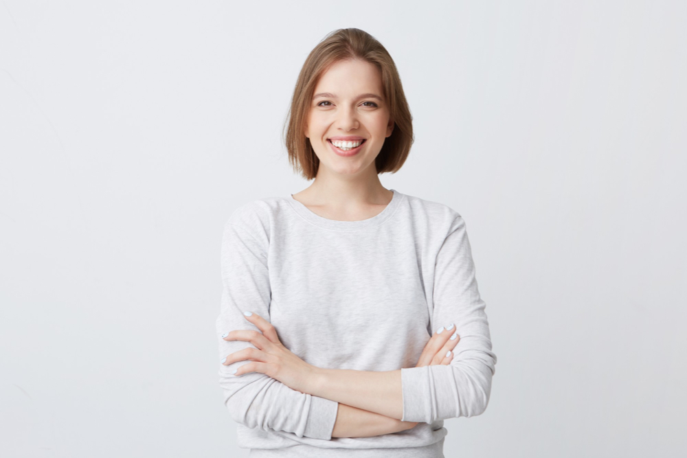 Cheerful attractive young woman in long-sleeve standing with arms crossed and smiling