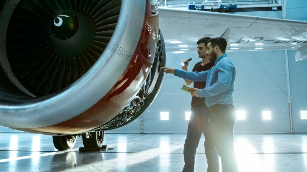 Two men standing in front of the turbine of an airplane 