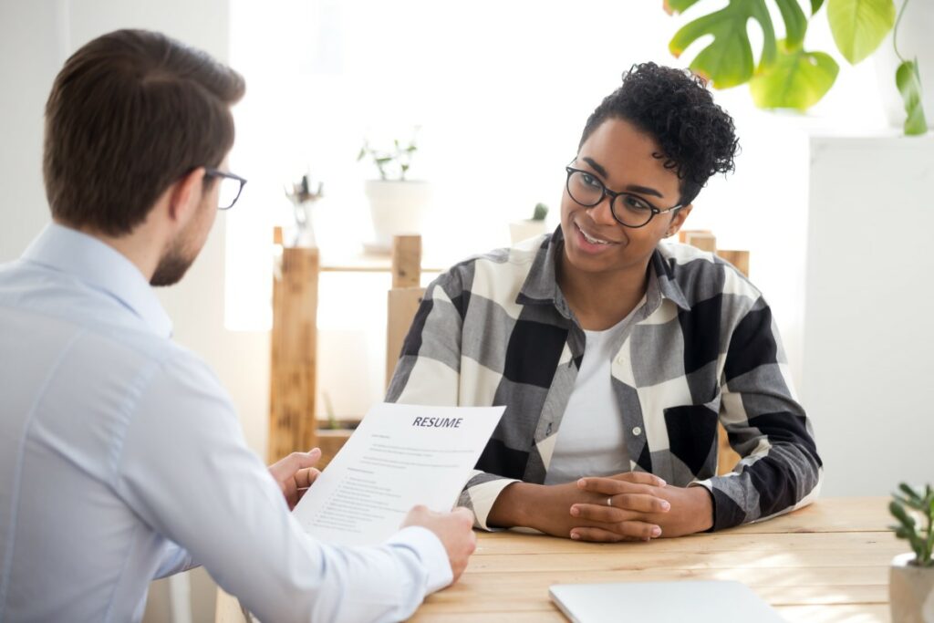 young person that applied for a job having a job interview smiling at the interviewer holding their resume