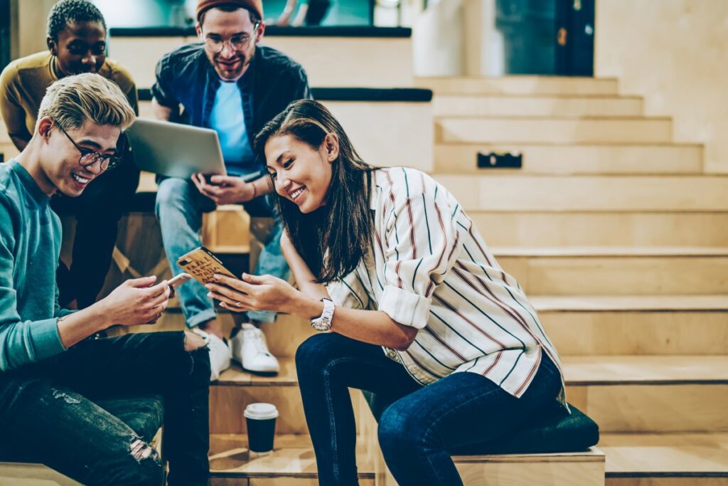 Young people checking their phones and laptops smiling and interacting 