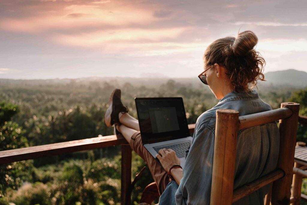 Young woman, Working on laptop, Outdoors, Sitting on chair, Relaxed mode, Wearing sunglasses, Sunset in the background