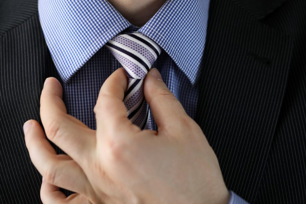 man tightening the knot on his tie with two fingers, preparing for a job interview, tie with purple, white and black stripes