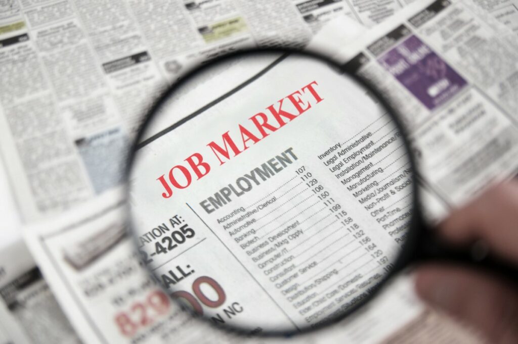 Newspaper with a magnifying glass above the job market and employment section in order to find a job