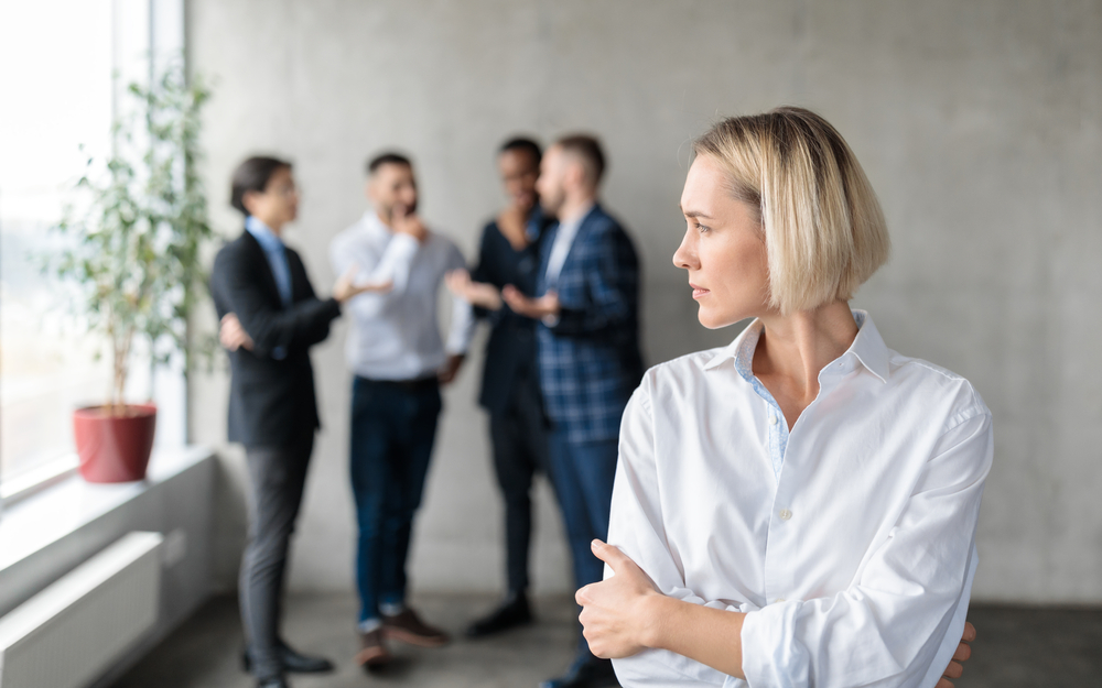 Male,Coworkers,Whispering,Behind,Back,Of,Unhappy,Businesswoman,Spreading,Rumors