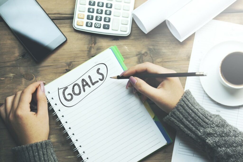 Hands of a woman noting down her goals at job search on a ruled notebook with the word goals in black capital letters 