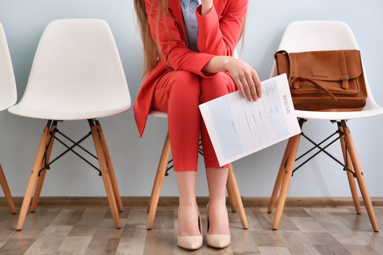 A woman that is dressed in red, sitting on a chari holding her resume in her right hand