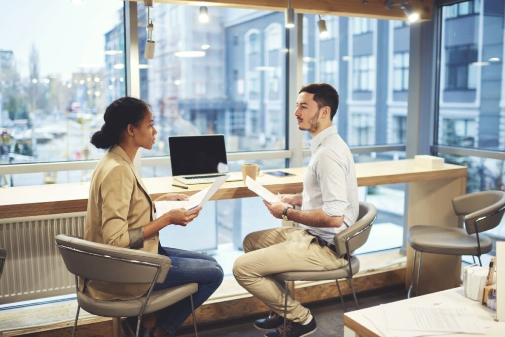 Two people sitting in chairs, wearing business clothes and holding paper in their hands