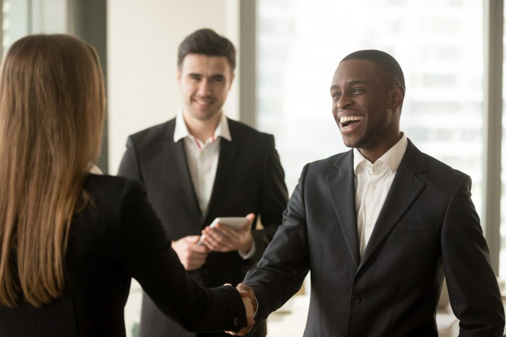 two person shaking hands after a perfect job interview. A third person standing in the background is smiling aswell.