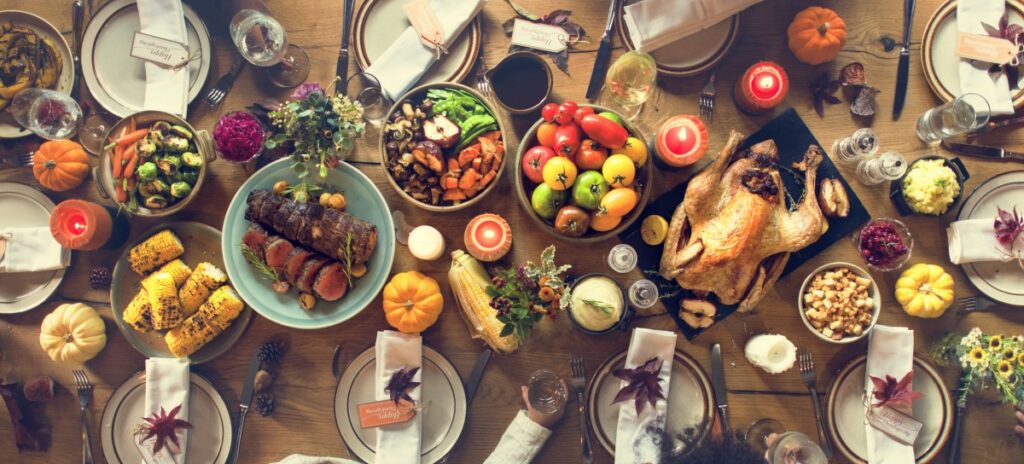 well-laid thanksgiving dinner table with stuffed turkey, fruit, vegetables, beef, corn, and more