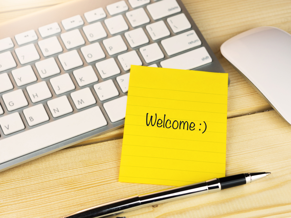 Welcome,With,Smily,Face,On,Sticky,Note,On,Work,Table