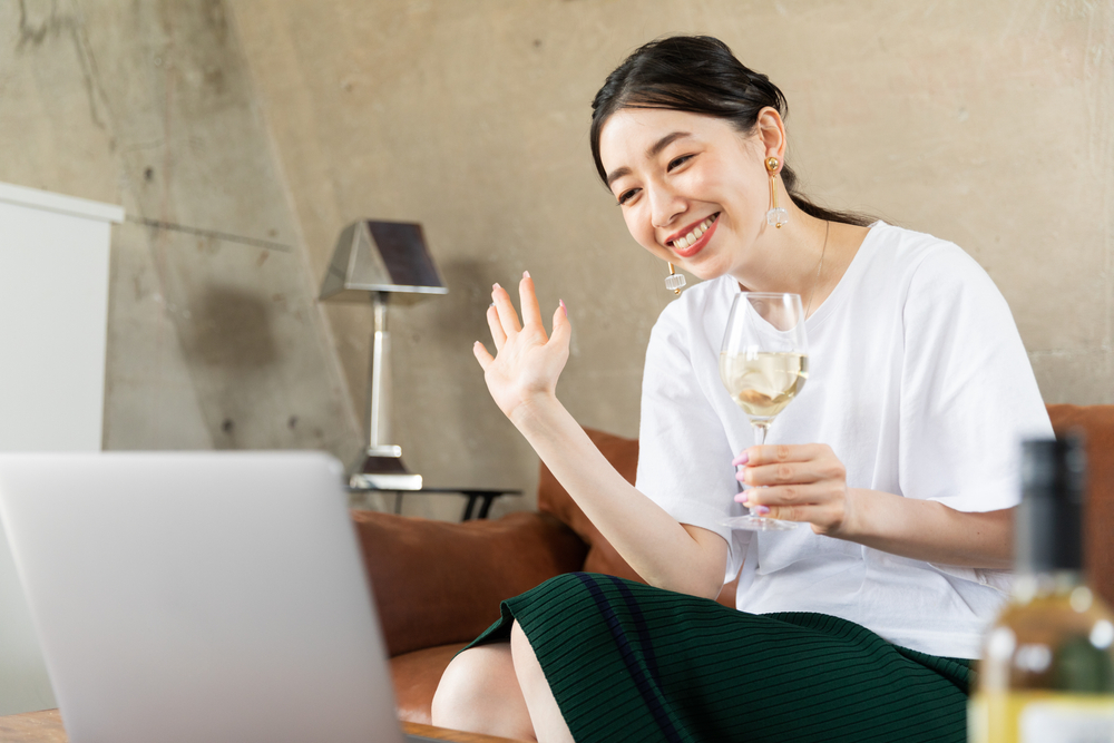 woman waving at laptop with glass in her hand